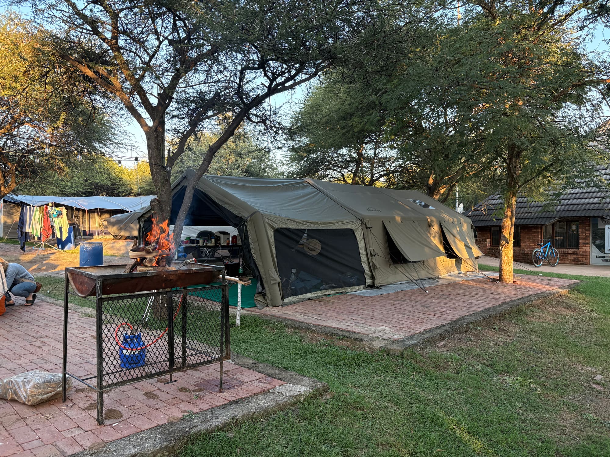 Braai fire burning at dusk in front of the Coody Familia tent at Dube, Brits, coody branding visible on the awning