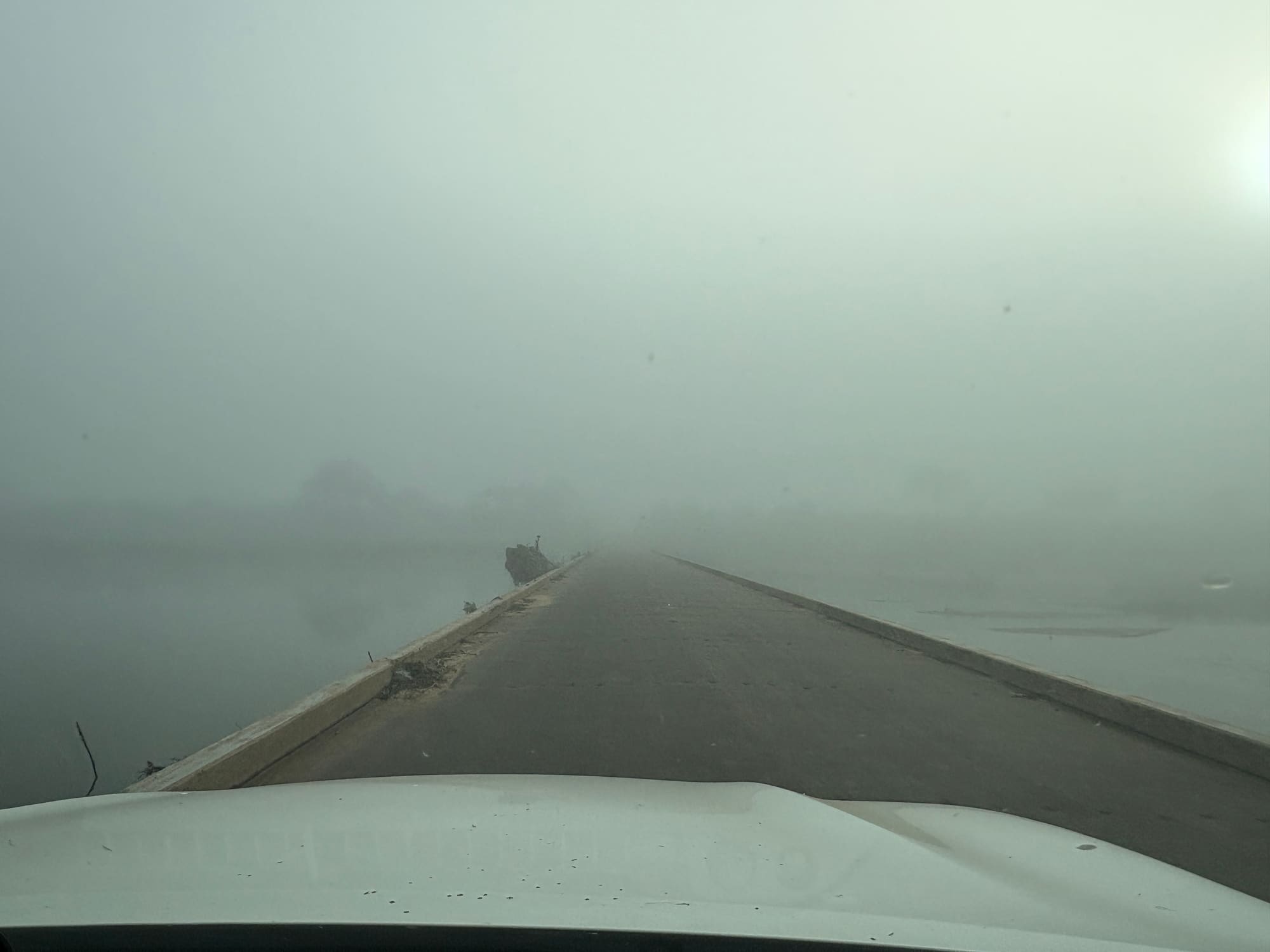 Thick fog over the causeway and water near Crocodile Bridge, Kruger National Park, seen from inside the car