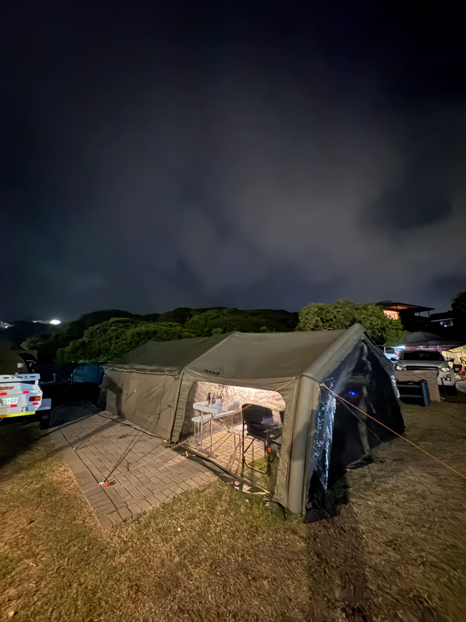 Coody Familia tent lit up at night, table and chairs set inside