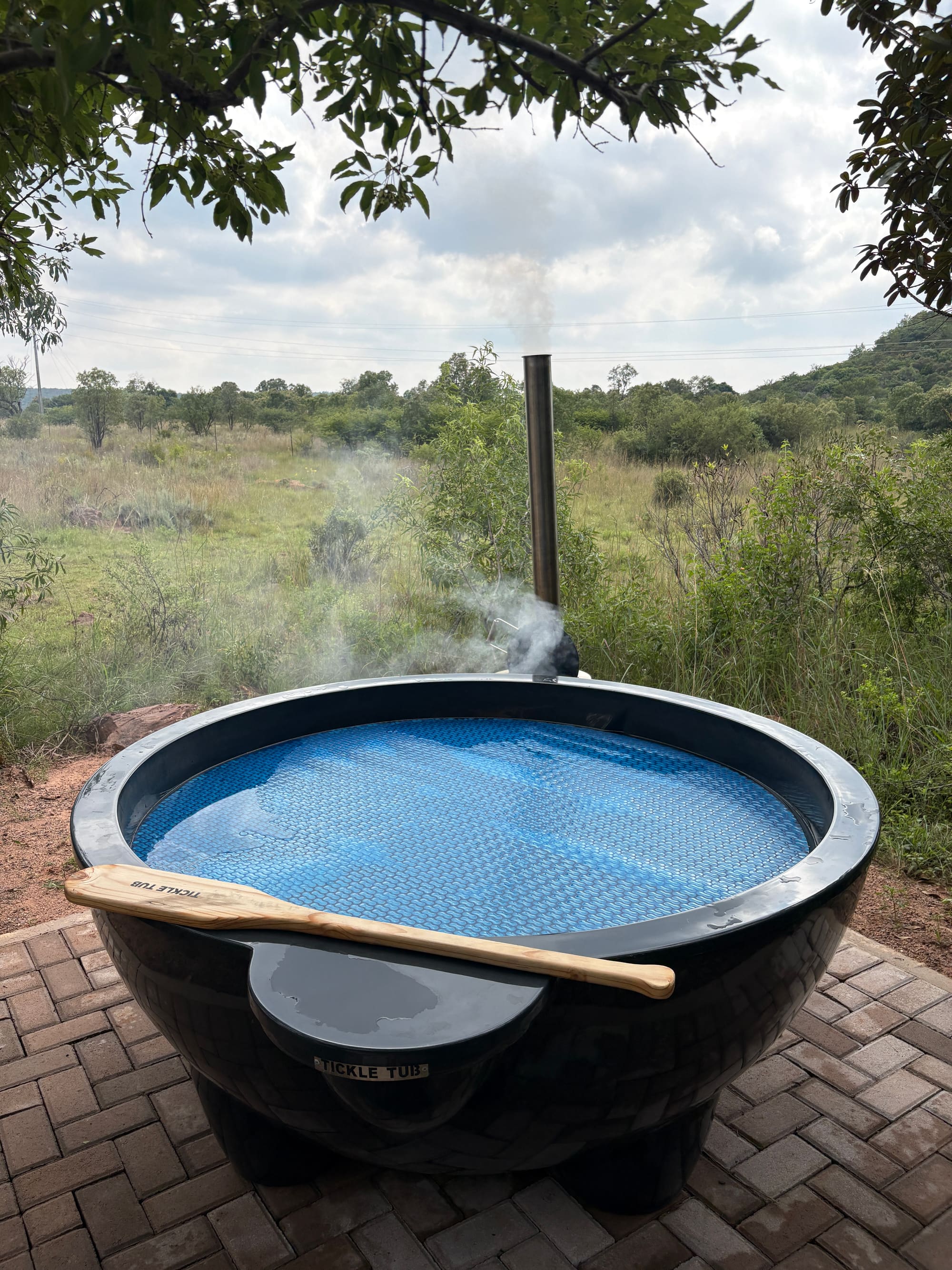 Close-up of the wood-fired Tickle Tub hot tub, steaming, with a wooden paddle resting on the rim
