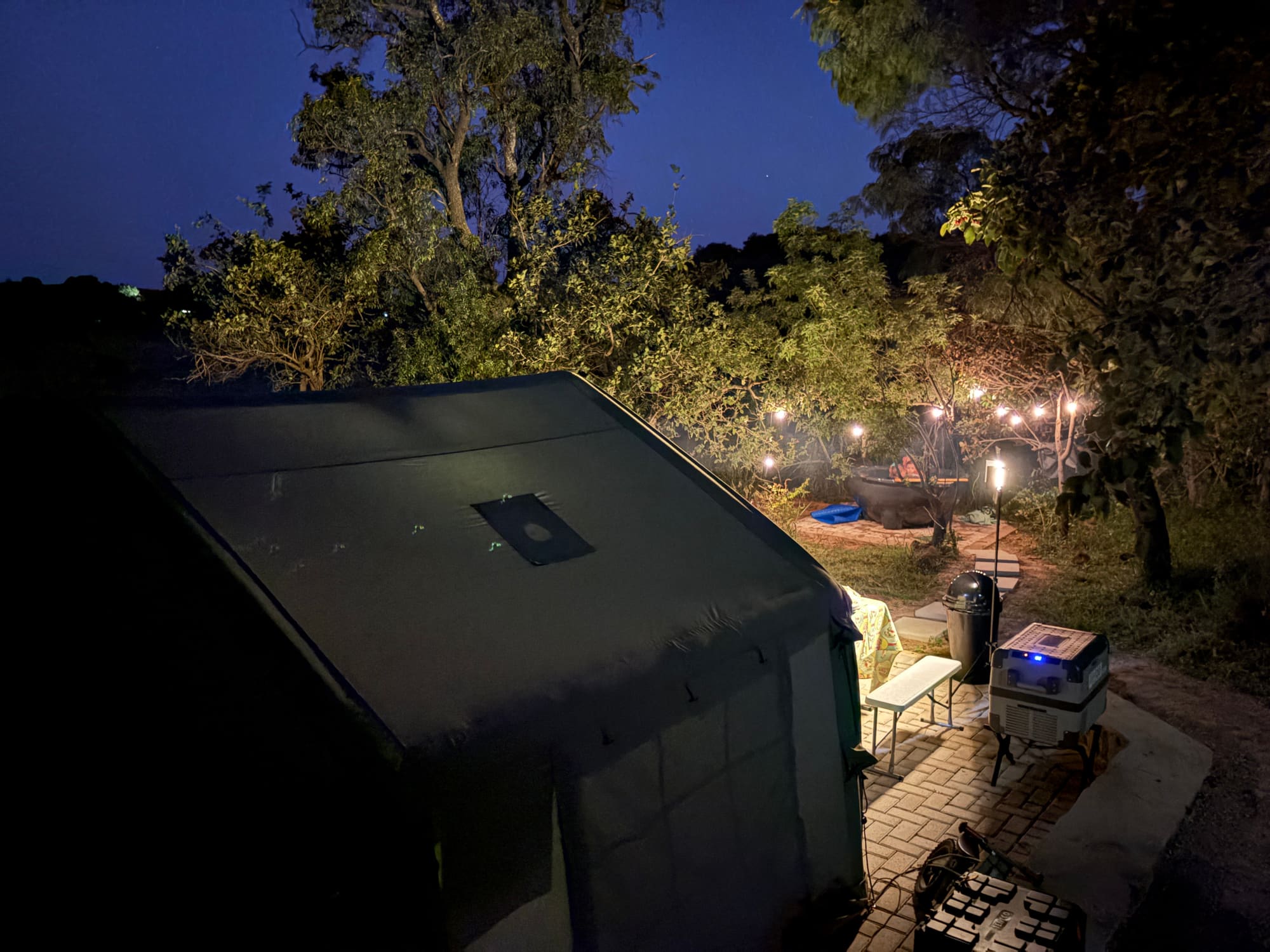 Dinner table set at night beside the Coody tent, fridge and chairs nearby