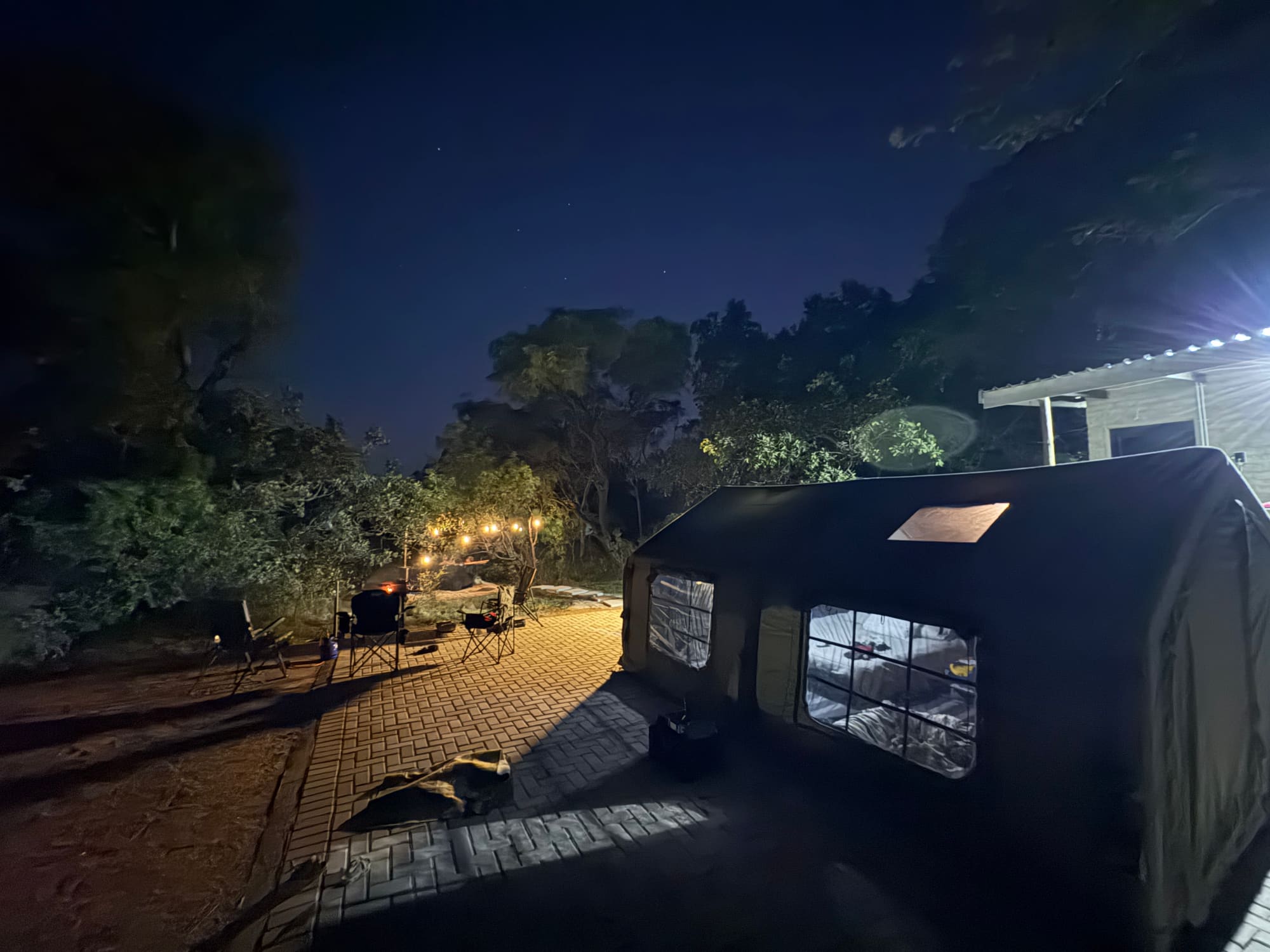 Coody tent at night, mesh windows lit, stone path leading past the campsite