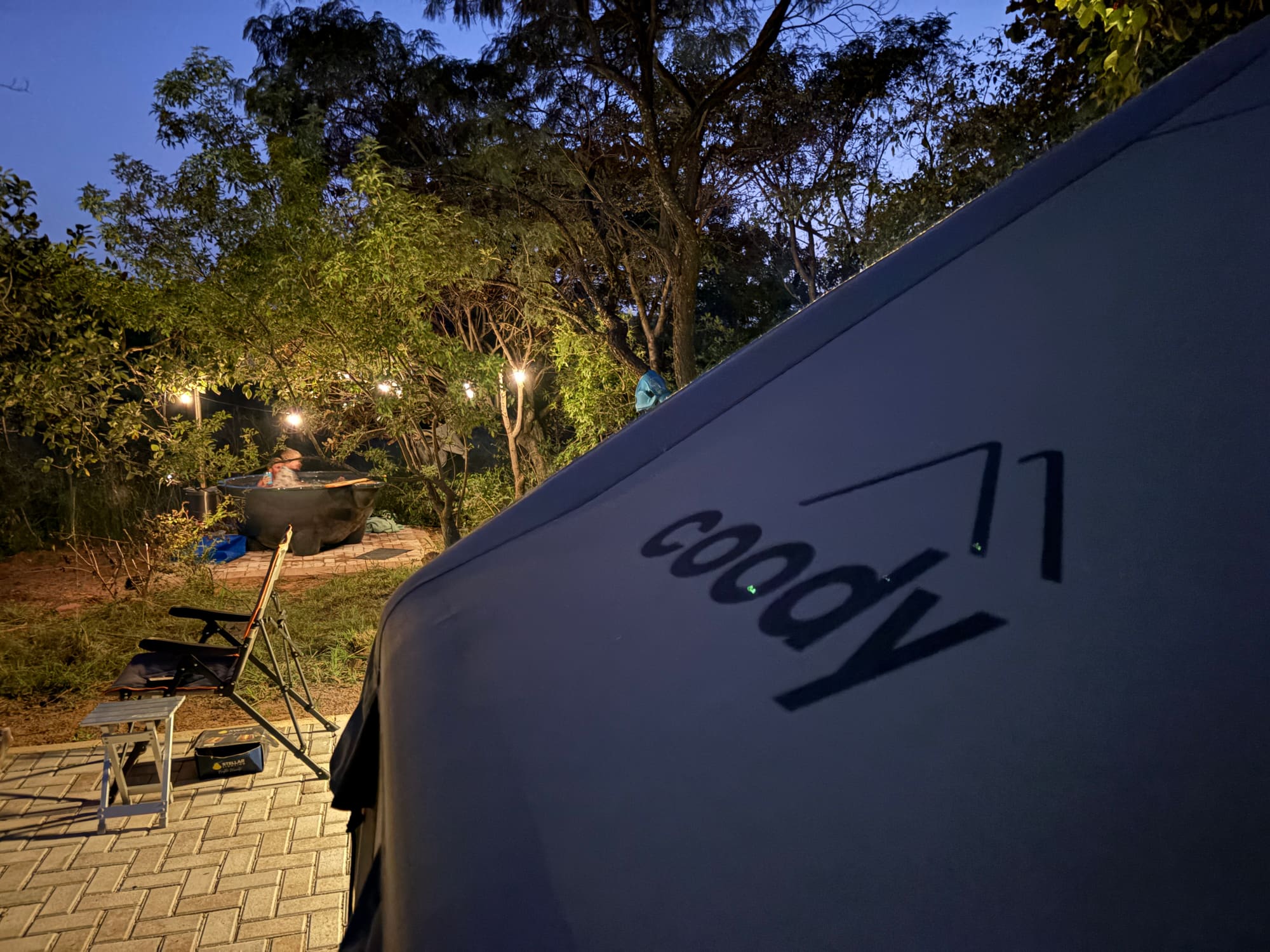 Coody branding close up at night with the hot tub and string lights glowing behind