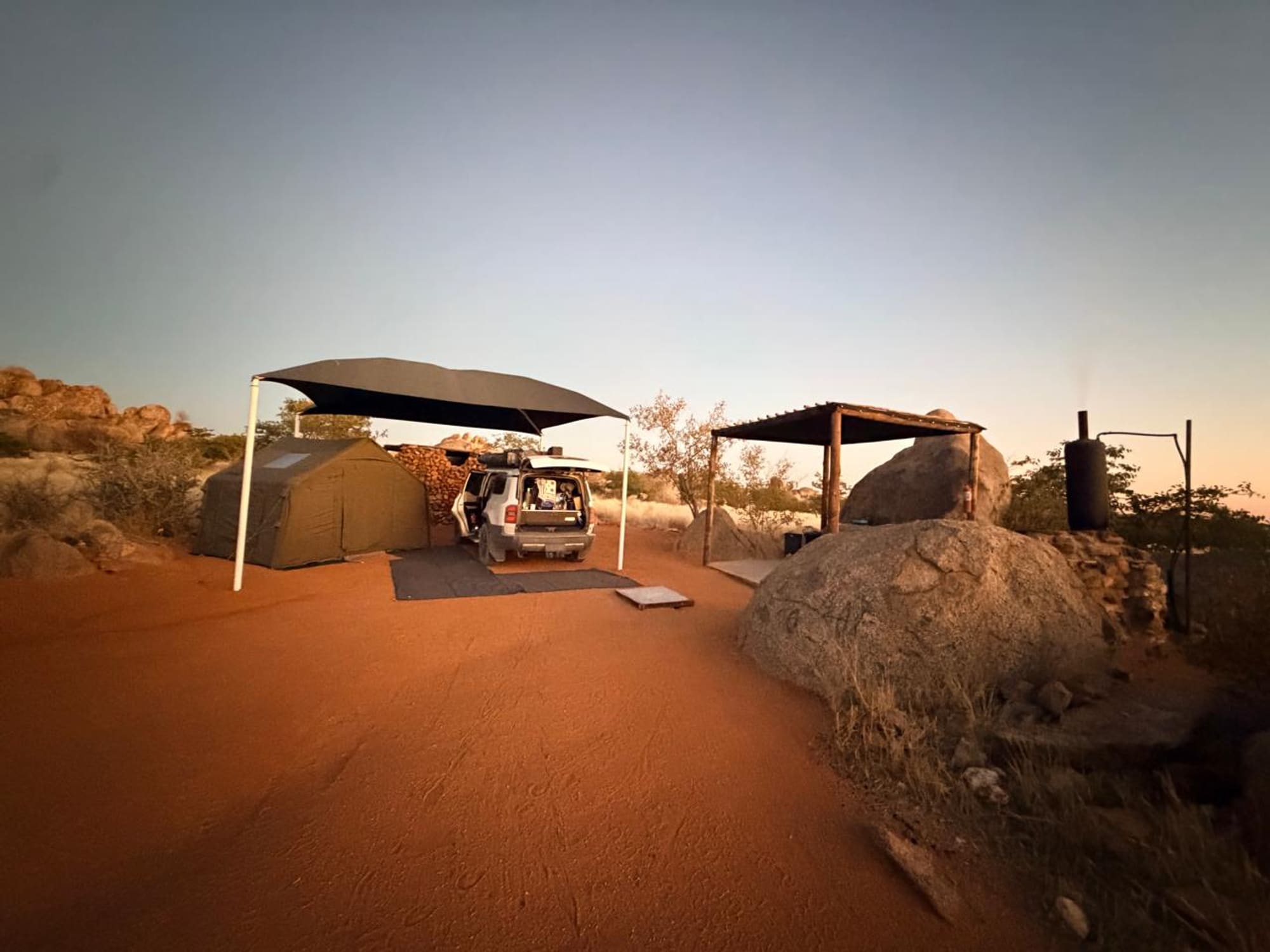 Coody 8 campsite at Hoada, Namibia, at dusk among granite boulders with a firewood stack and shade shelter