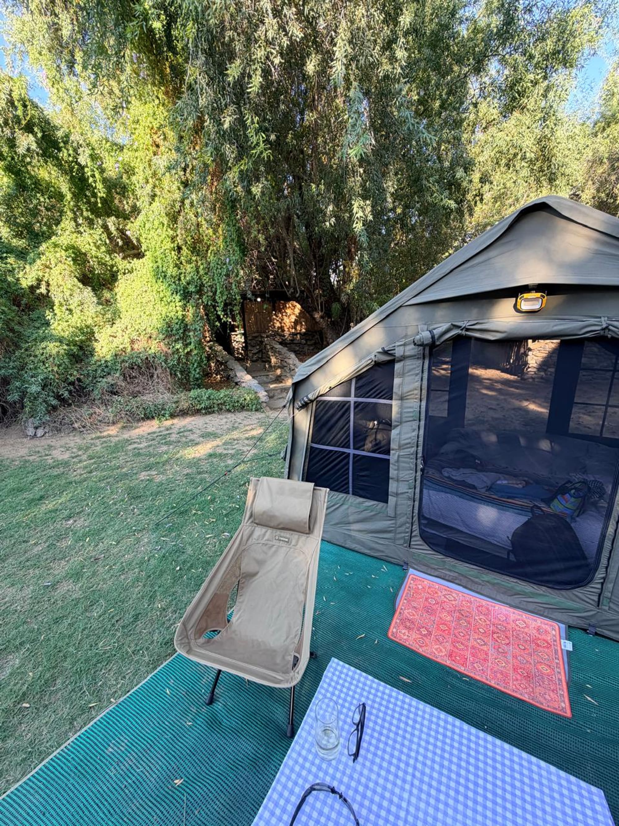 Coody 8 tent on the banks of the Orange River, camp chairs and table set up outside under willow trees