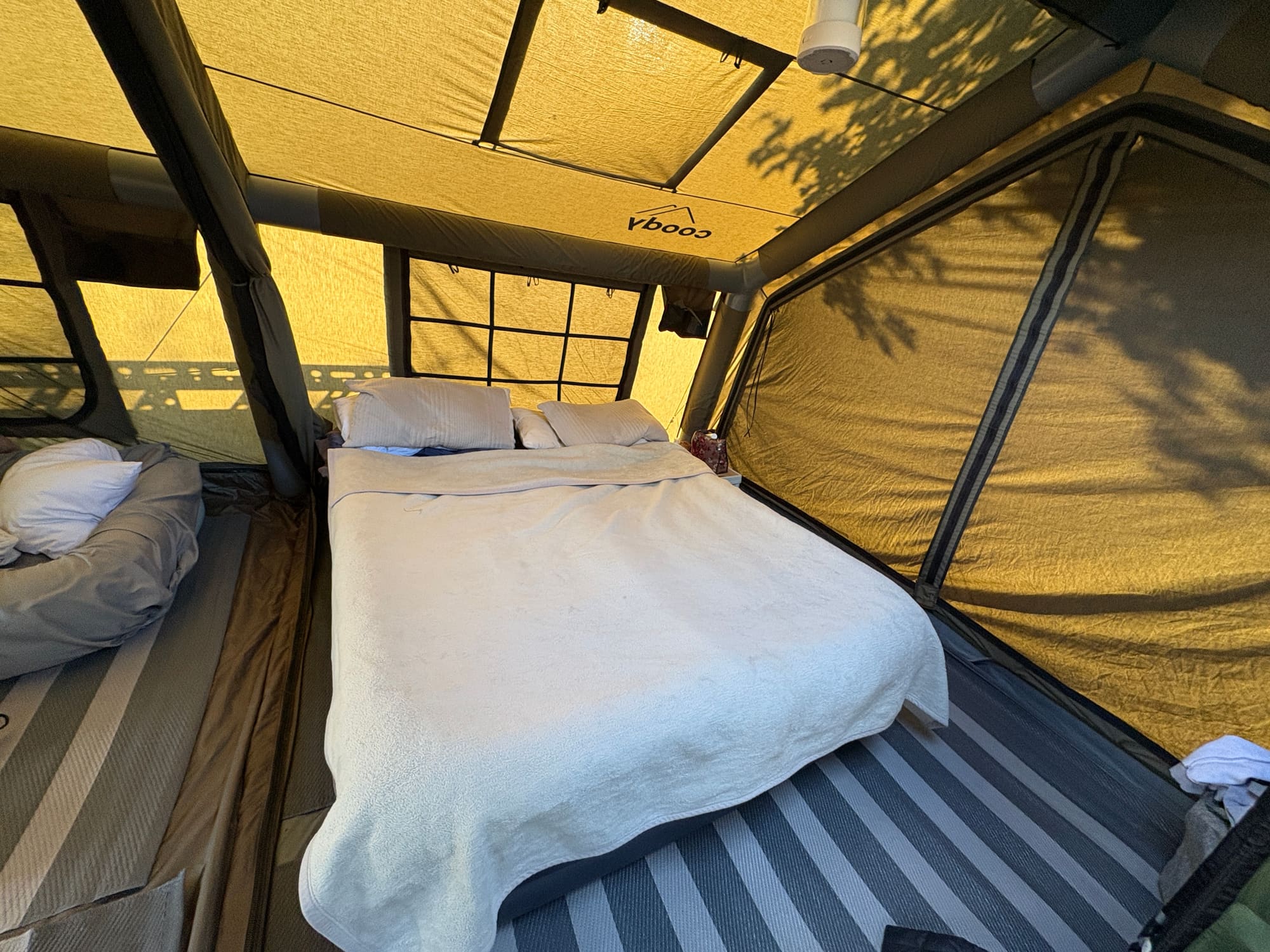Interior of the Coody Familia tent at Satara, double bed made up with white bedding, coody branding visible on the ceiling