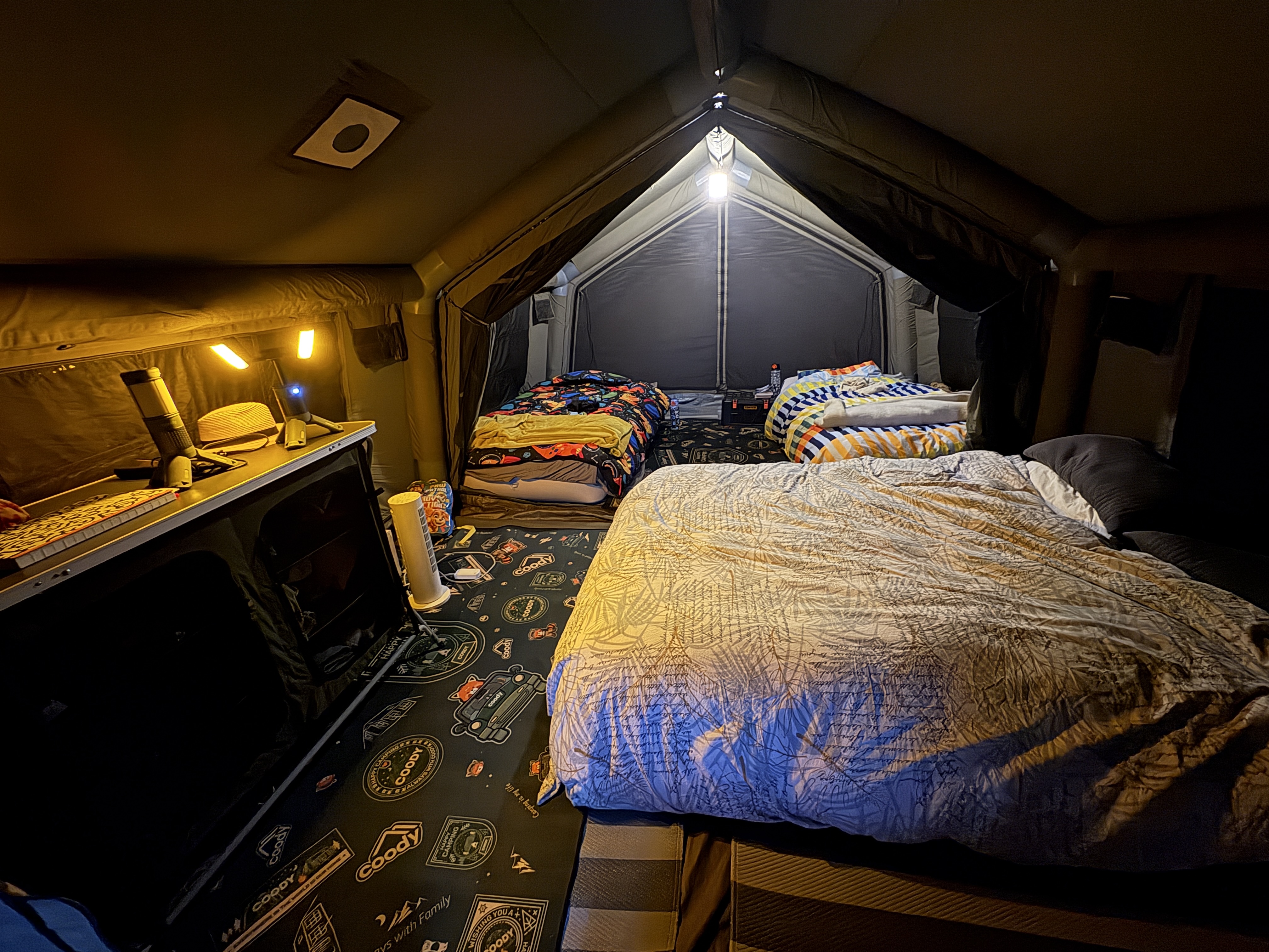 Inside Chris's Coody tent at night, two kids' beds and a double bed set up cosy and lit up